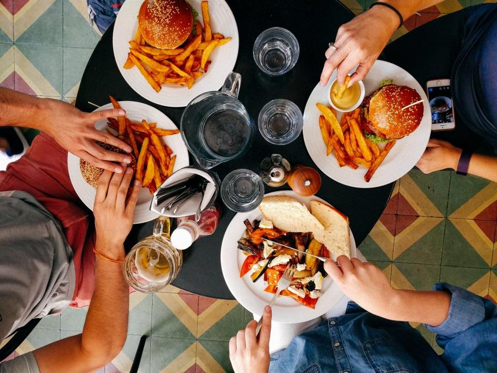 Friends sharing burgers, chips and other dishes at a restaurant table, seen from above.