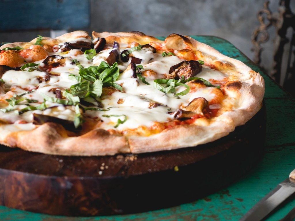 An Italian pizza with cheese and vegetables on a wooden board in a restaurant.