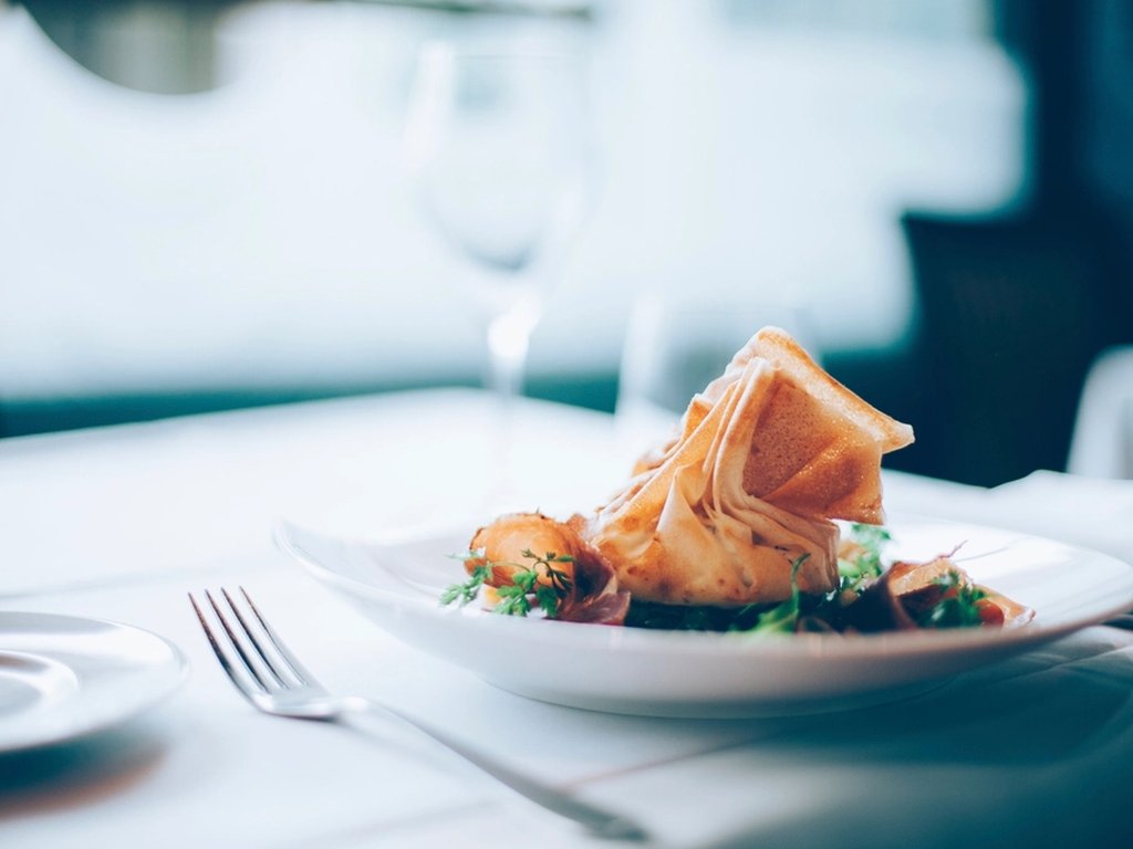 A beautiful plate of food on a white tablecloth in an expensive restaurant.