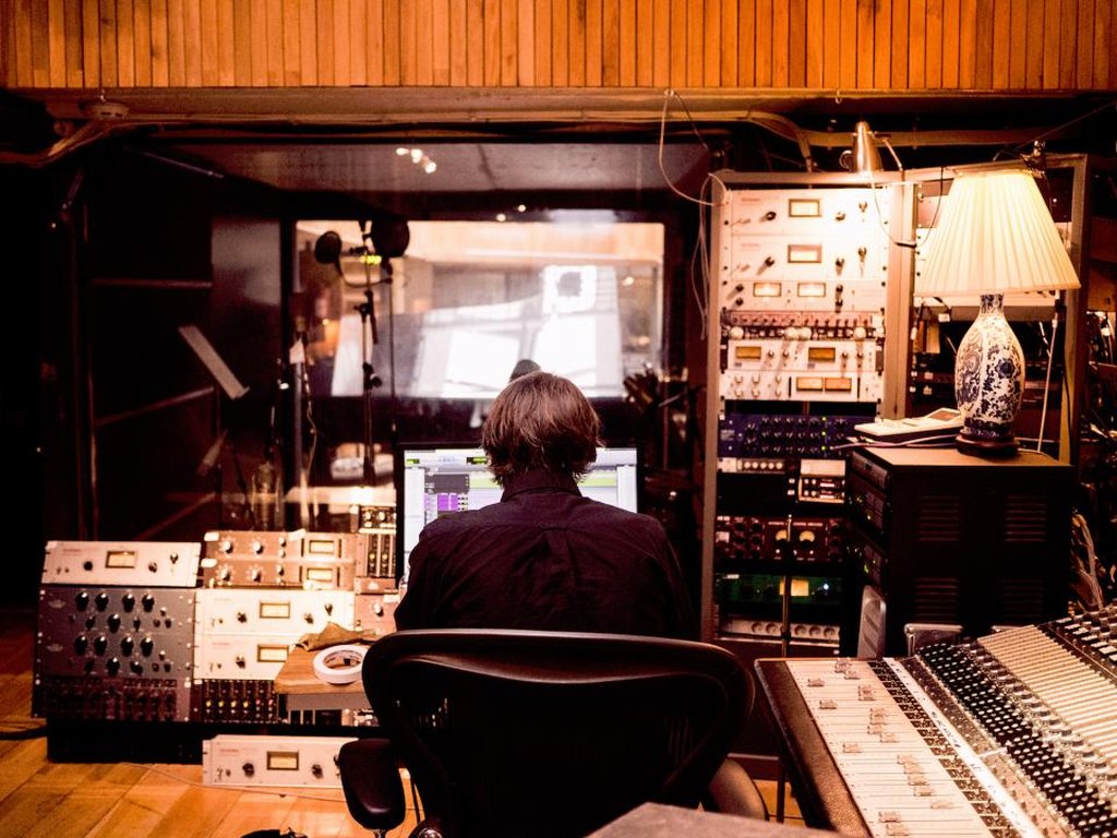 A sound engineer at a desk full of recording equipment in a studio.