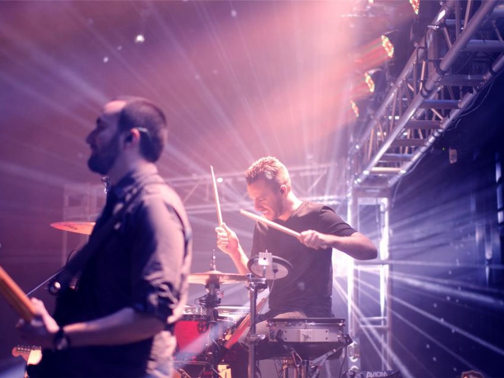 A guitarist and a drummer on stage under bright lights at a live show.