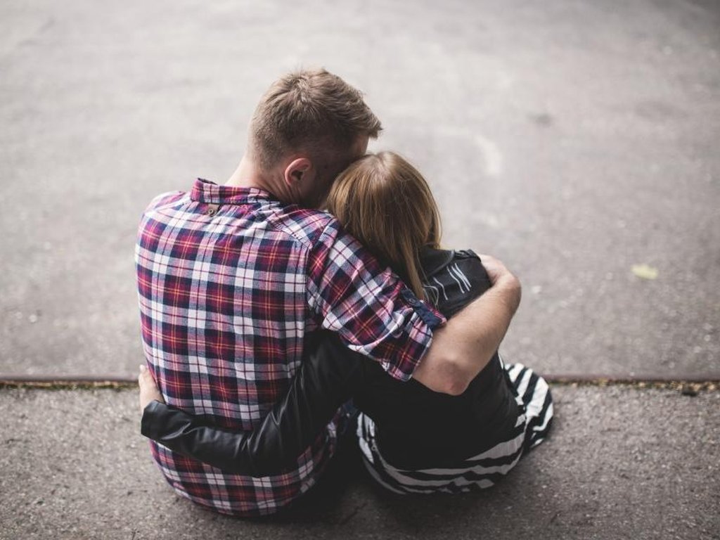 Two people sitting on the ground, one with his arms around the other.