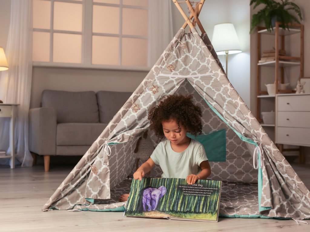 A young child looking at a picture book inside a play tent at home.