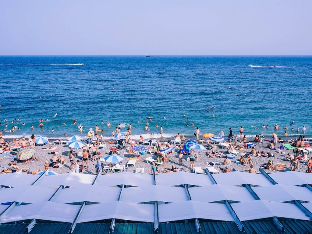 A beach packed with people swimming and sunbathing on a hot summer day.