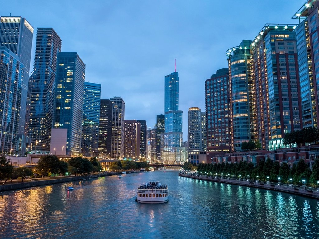 A sightseeing boat full of tourists on the river in Chicago, between tall skyscrapers.