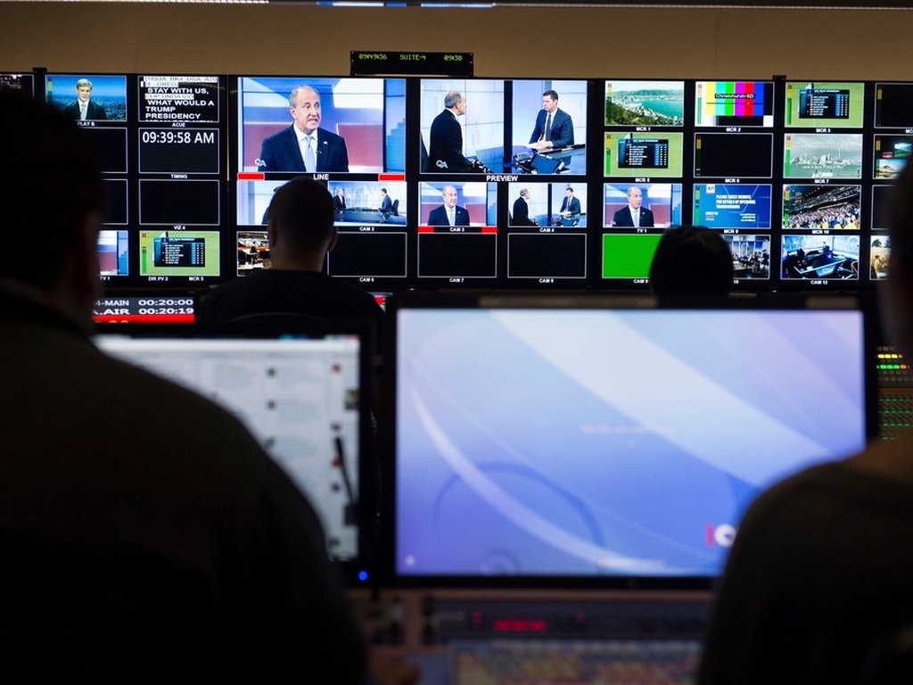 A TV control room with a wall of screens showing the news.