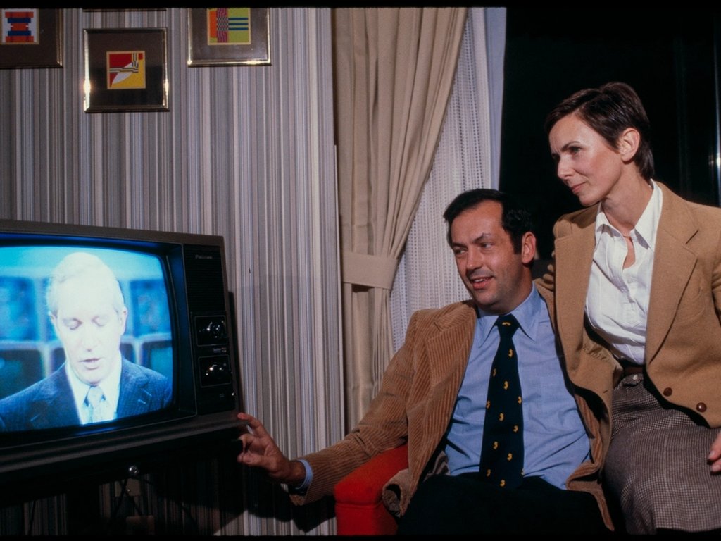 A couple watching the news on an old television at home.