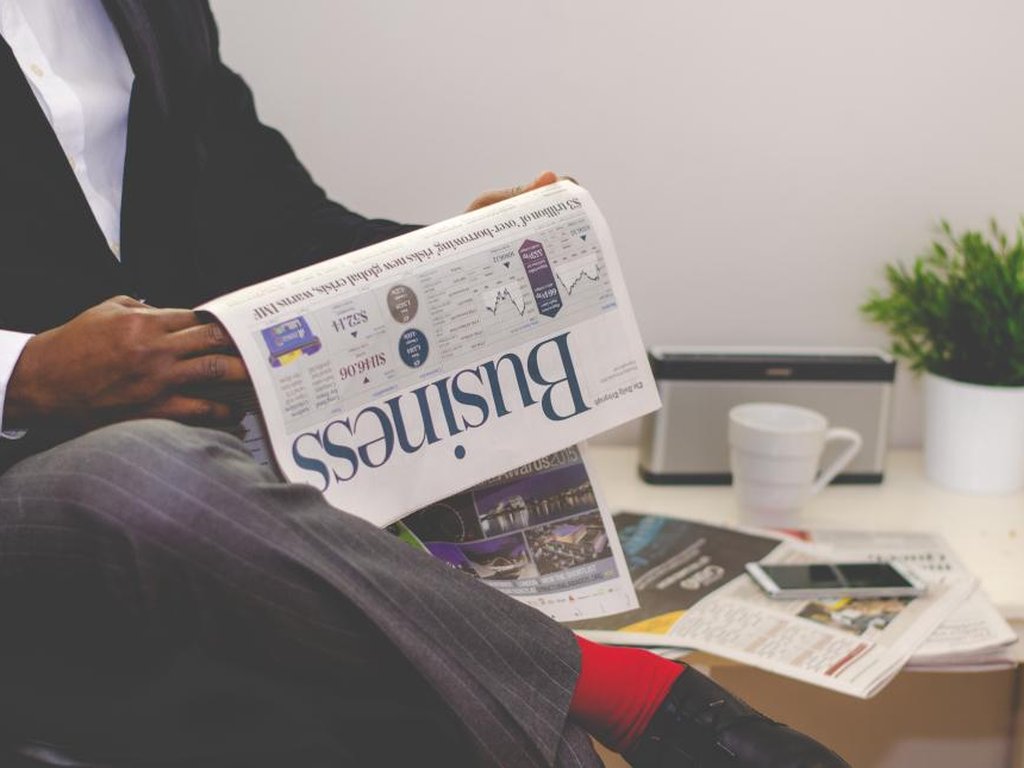 Someone reading the business pages of a newspaper, with a coffee on the table.
