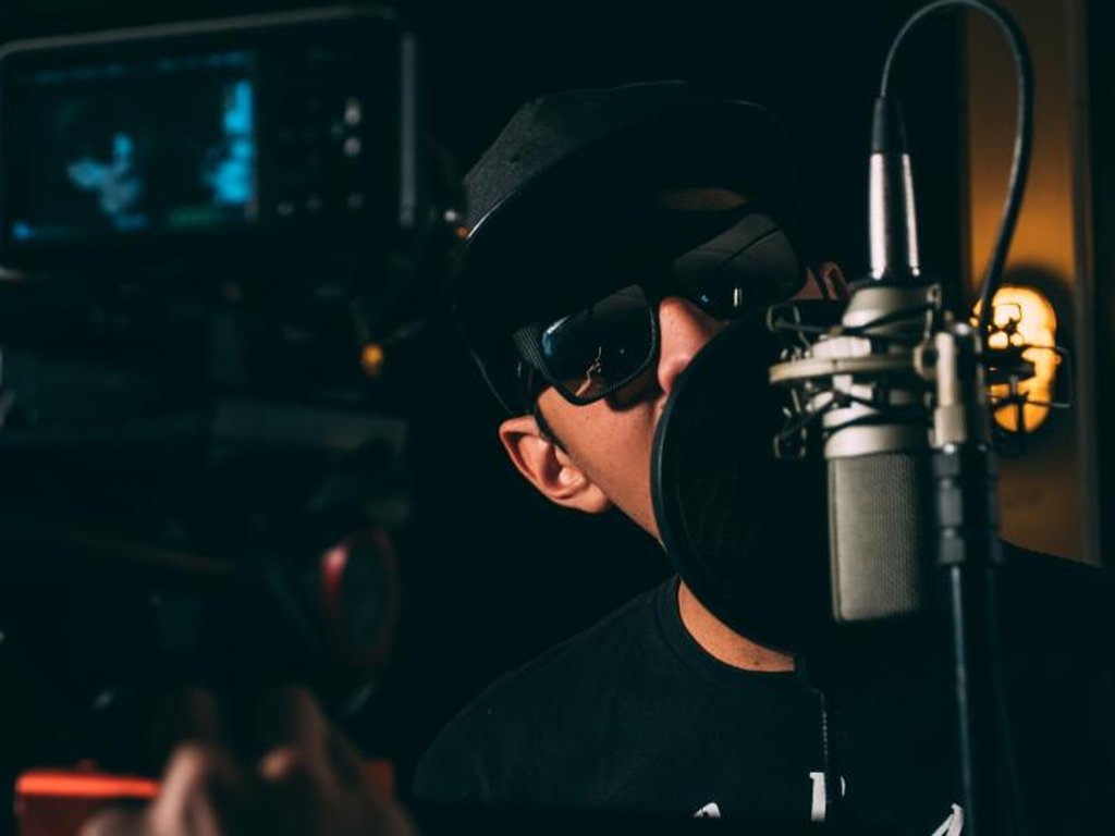 A young man speaking into a studio microphone, maybe for a podcast or an online video.